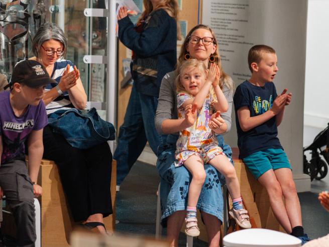 Group of people watching a show all smiling and clapping their hands.