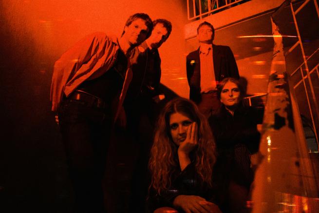 the members of Delivery stand on steps in red lighting