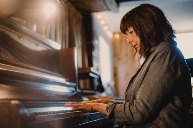 Emily sat at a wooden piano, focused whilst playing it