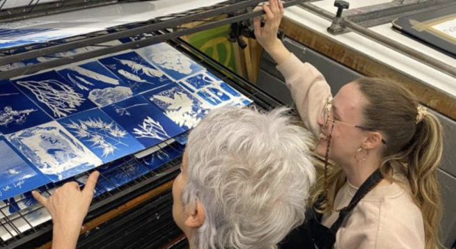 Two artists looking at a selection of cyanotypes drying on a drying rack