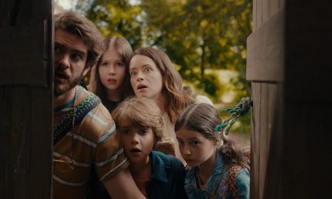 A family, a man, three children and a woman peer around a doorframe with shocked faces