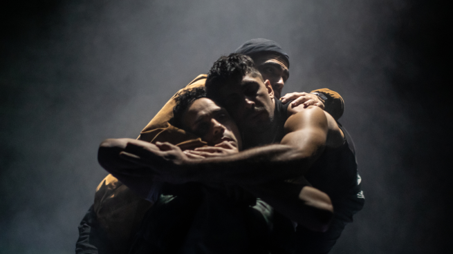 Three men embrace with their arms around each other. 