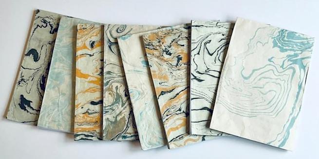 A selection of marbled paper in shades of blue, orange and cream laid out on a white background.
