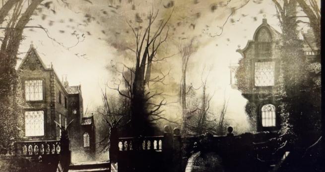 A black and white blurred image, featuring bare trees, and two spooky looking old buildings.