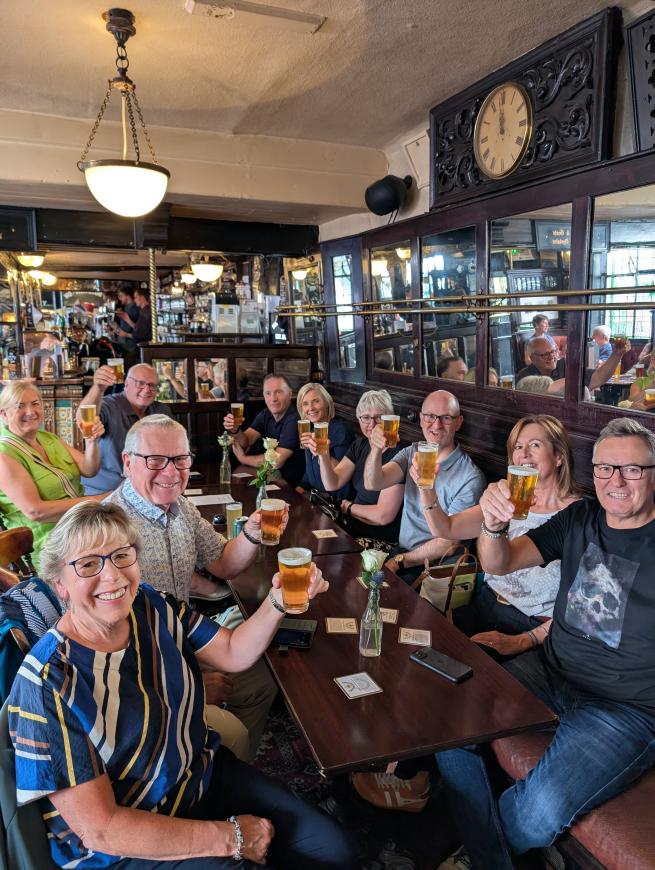 Tour guests inside a pub, raising beer glasses to the camera