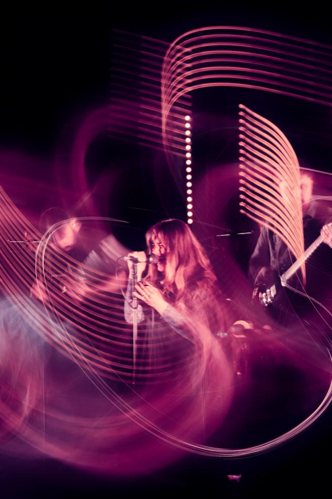 a blurry photograph of a singer with a microphone and 2 guitarists beside them