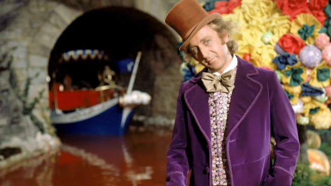 Man with brown top hat and purple jacket in front of tunnel with blue boat inside