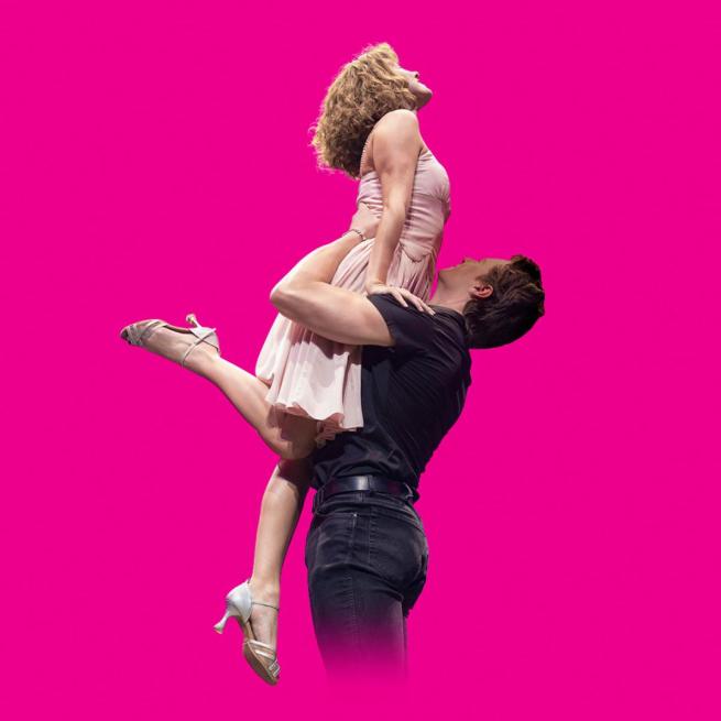 Shot in profile against a bright pink backdrop, a male dancer in a short-sleeved black shirt and dark hair raises up a blonde female dancer, wearing a pale dress and heels, one foot pointing out.