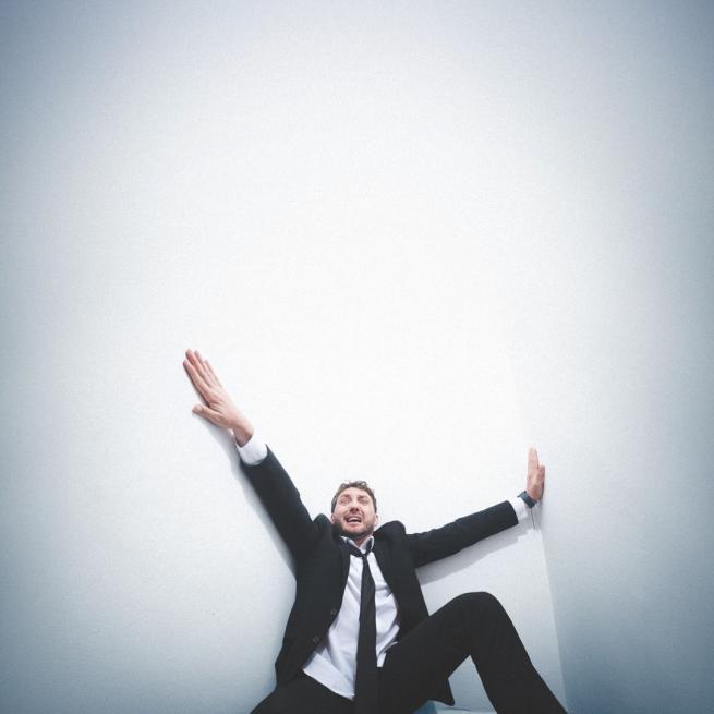 Looking panicked in the corner of a white room, Seann Walsh holds onto the walls with stretched arms and legs.