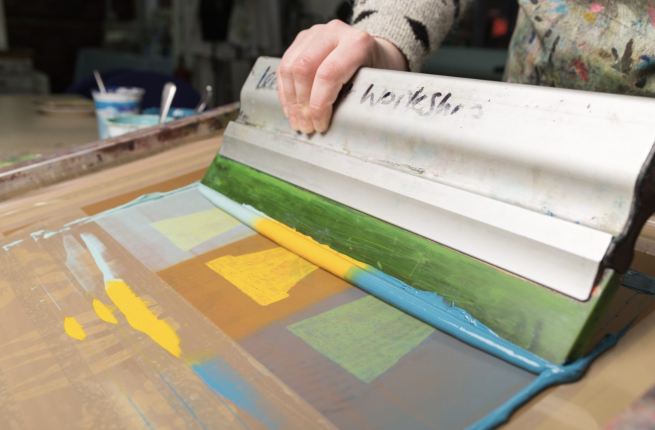 A squeegee being used to screen print images of plant pots in blue and yellow inks