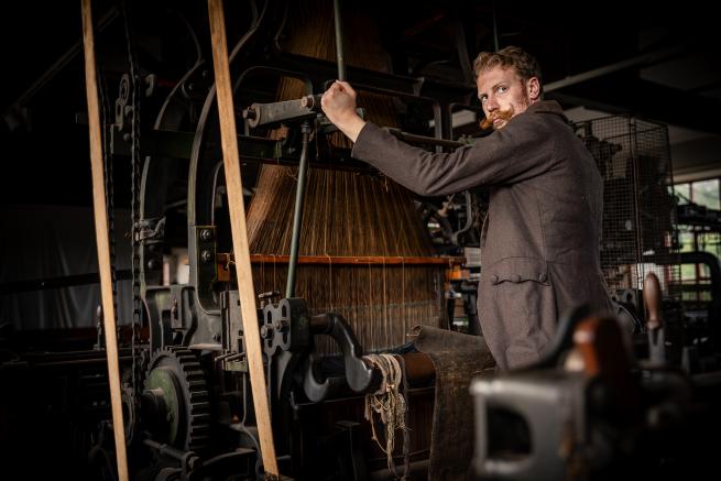 a man with a large moustache in a brown jacket using a large industrial machine in Leeds Industrial Museum