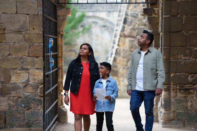 Two adults and a child walking through a stone gateway and looking around in Kirkstall Abbey