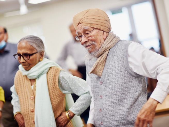 A man and a woman dance next to each other smiling with their hands on their hips 