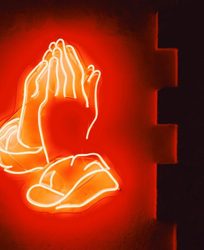 A red neon hand praying
