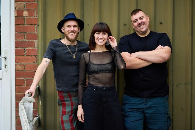 The makers of the show, two men and a woman are standing, smiling at the camera.