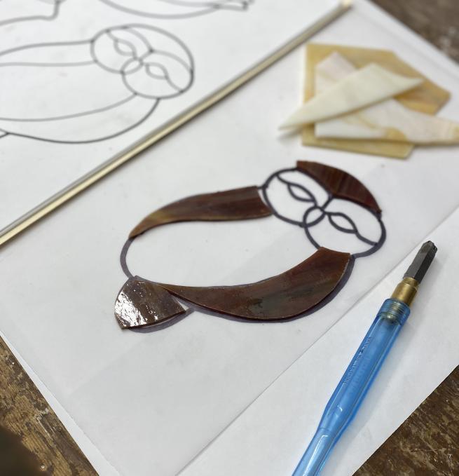 A photograph of some brown glass laid on top of an owl paper template