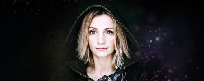 A women with medium length light coloured hair, wearing a black hooded robe.