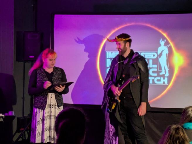 two people on a stage, one holding a book, another holding a guitar
