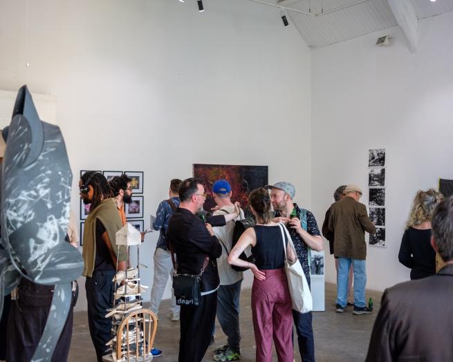 A group of people can be seen in a gallery space, surrounded by wall hangings