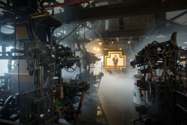 Photograph of a factory with industrial machinery, with ambient smoke obscuring the background.