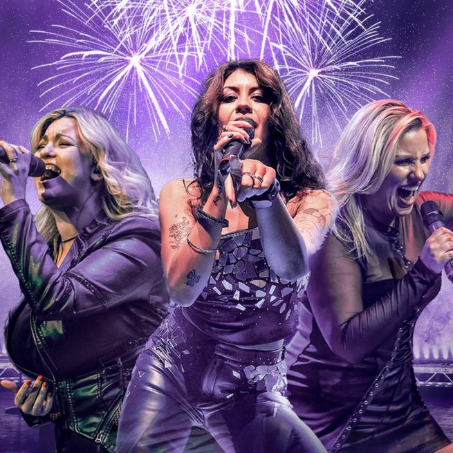 Three women sing into handheld microphones, surrounded by purple haze and fireworks.