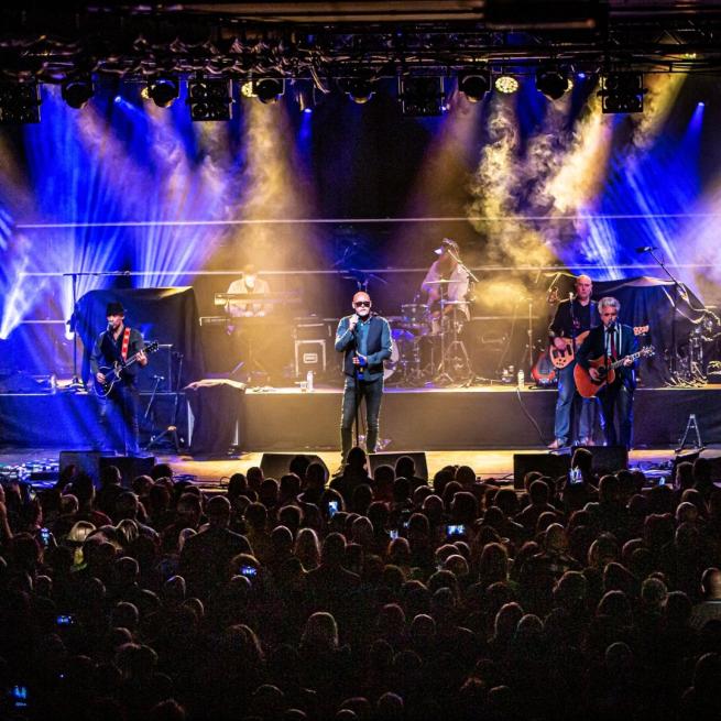 The Christians perform onstage to a packed crowd, lit by blue and yellow spotlights.