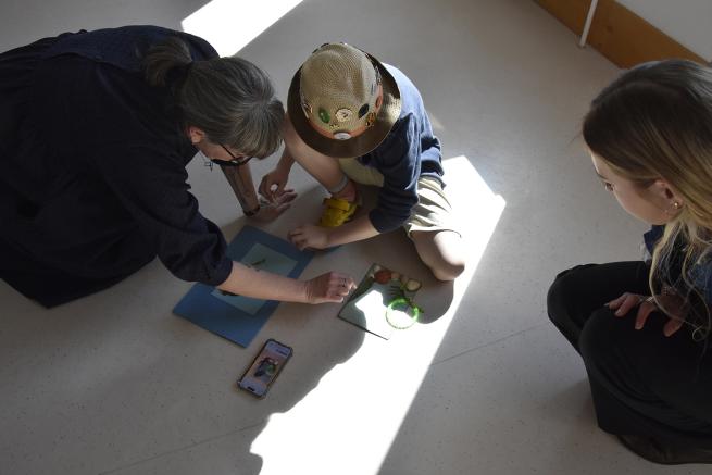 Two adults and a child working together to make a collage artwork on the floor.