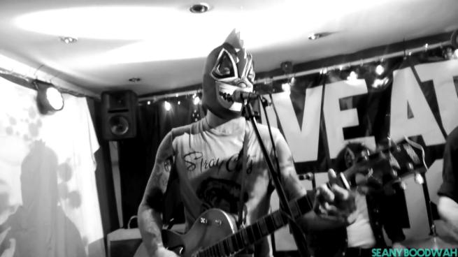 A black and white image of a man playing guitar with a spooky mask on.