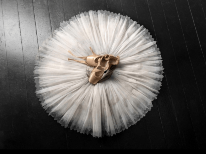Image of a tutu and a pair of pointe shoes on a dark wooden floor