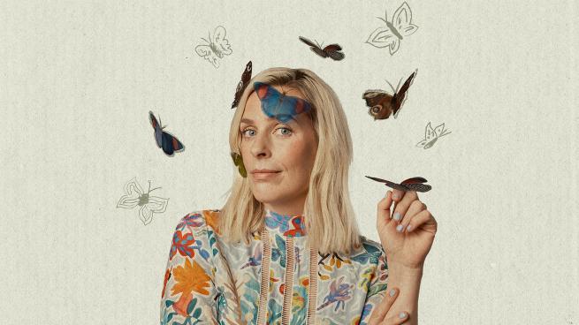 A blonde person with shoulder length hair is surrounded by butterflies.