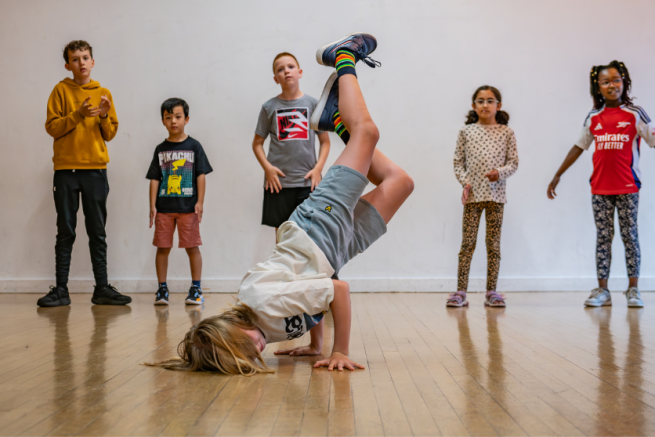 A child is street dancing in a freeze. Their balanced on their head and hands with their feet in the air.