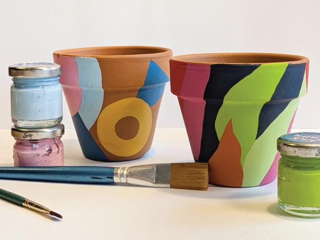 Two hand painted paint pots with bright patterns. Paint pots and brushes nearby