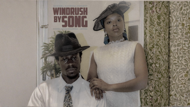 An image of two people wearing 1940's clothes. One is sat down wearing a hat and white shirt with a tie. The other is standing wearing a white dress, with their arm on the other person's shoulder. There is text above that reads 'WINDRUSH BY SONG'.