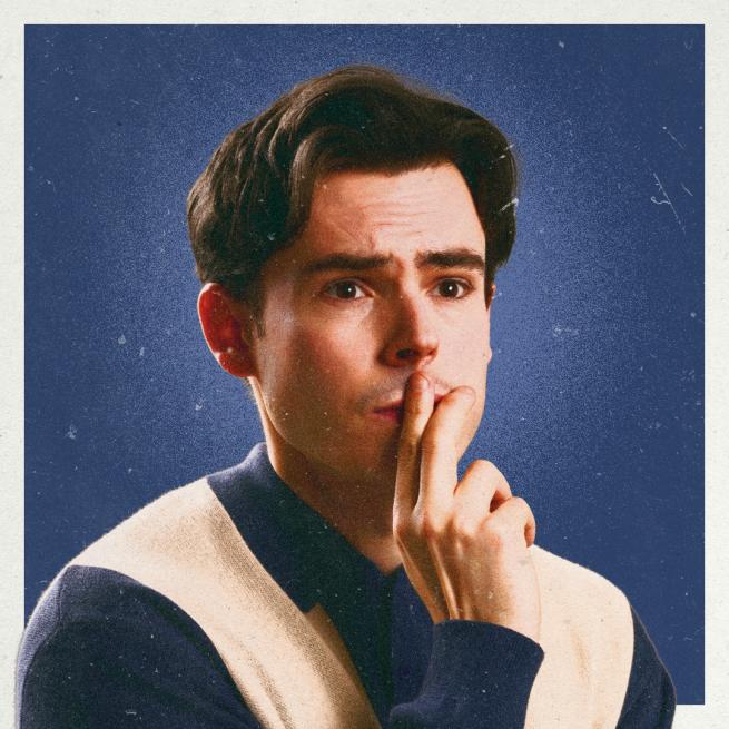 Rhys James looks pensive and holds two fingers to his lips, photographed against a blue backdrop with grain applied over the top.