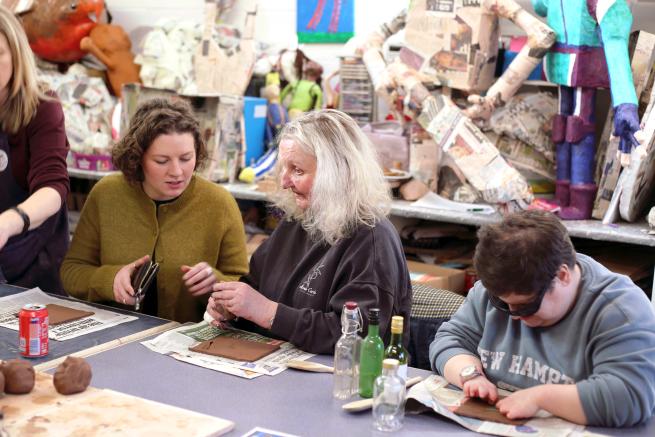 Within the art room at Henshaws, three artists sit at at table working on their craft. The room is filled with papermache models ready to be painted.