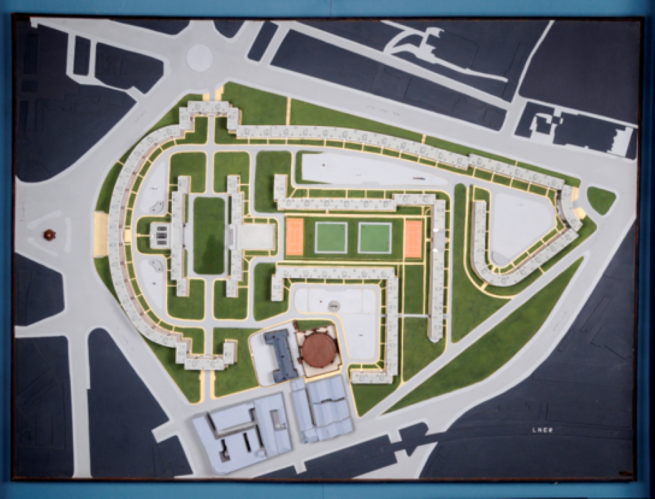 Overhead architectural site plan showing a large housing estate within a triangular block bordered by roads. Curved and linear residential buildings surround central green spaces, with tennis courts, pathways and service buildings arranged across the landscaped site.