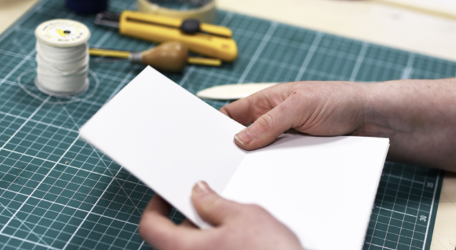A book being hand made, alongside thread and bookbinding tools