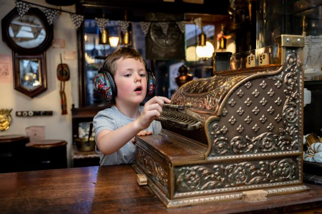 Child wearing ear defenders plays with an ornate old fashioned shop till