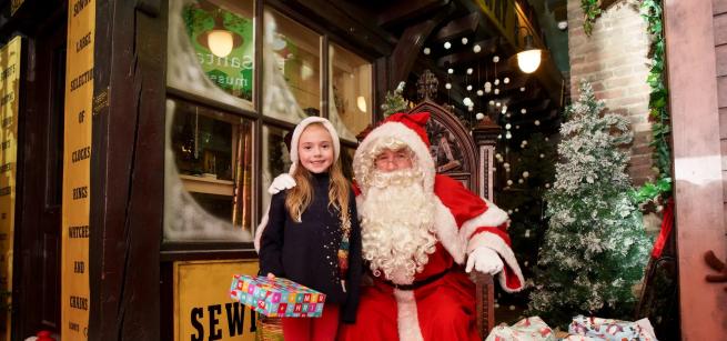 A colour photograph of a child in a seasonal outfit posing with Santa in the Victorian Streets at Abbey House Museum