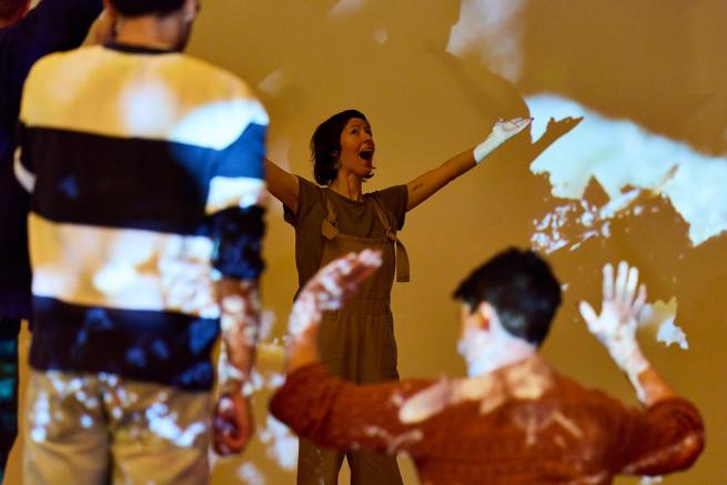 A woman holds her hands up in the air as part of a performance surrounded by children
