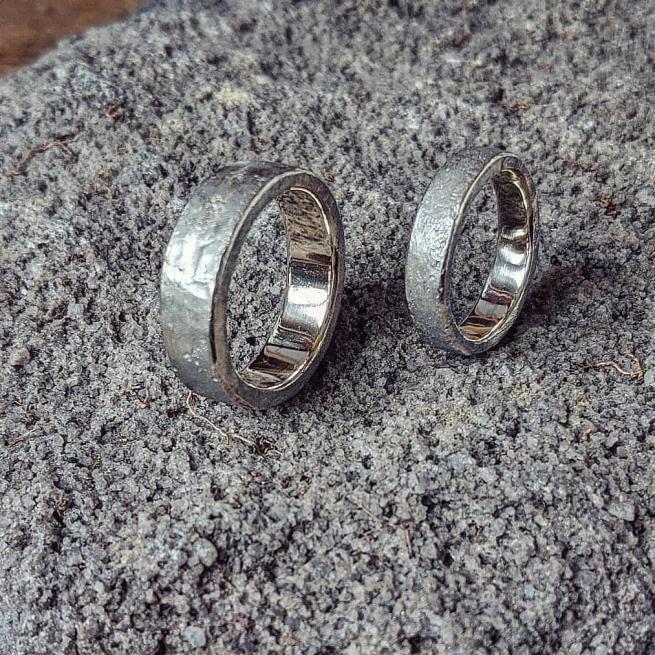 Two silver rings stand on their outer edge, on a grey fluffy surface. they are chunky with texture on the outside and a smooth inside.