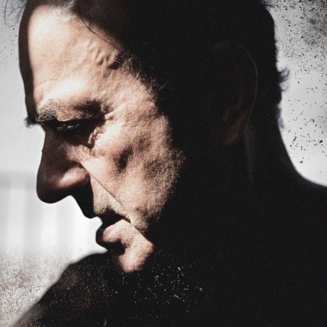 In profile under a harsh spotlight with dramatic shadows, Hugh Cornwell tilts down his head, with a gritty, textured filter. 