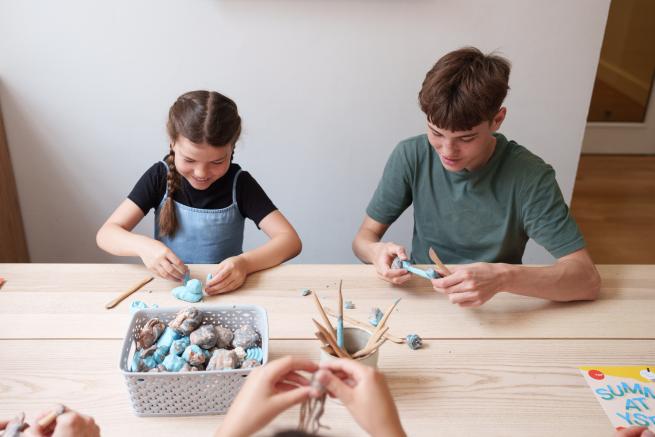 A girl and a boy sit at a table moulding with clay