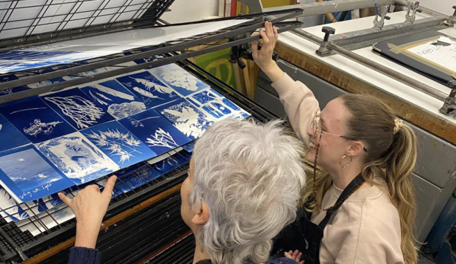 Two artists looking at a selection of cyanotype prints on a drying rack.