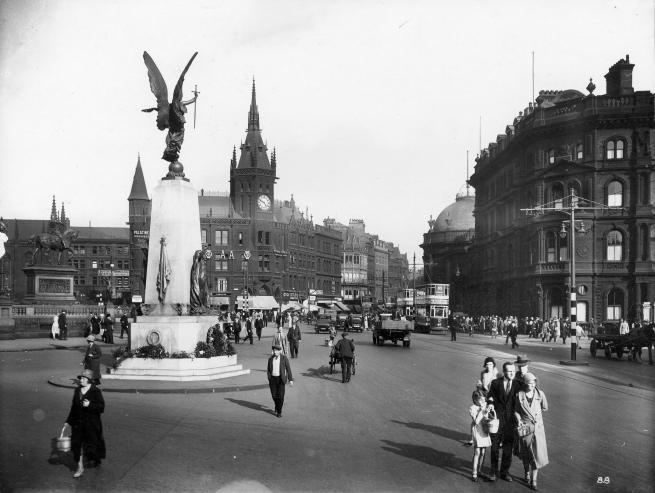 Black and white photograph of a busy street in Leeds with the war memorial in view.