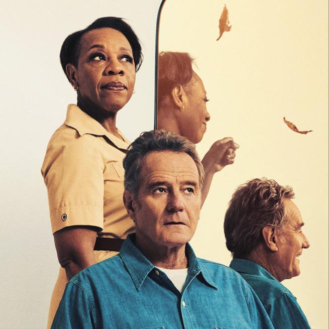 Bryan Cranston sits in front of a standing Marianne Jean-Baptiste, both with neutral expressions, contrasting their smiling faces in the mirror next to them. 