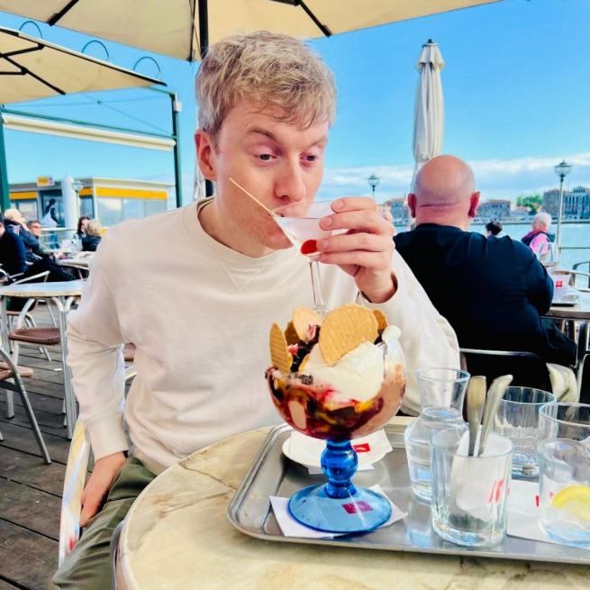 James Acaster sips a martini at a beach-front restaurant.