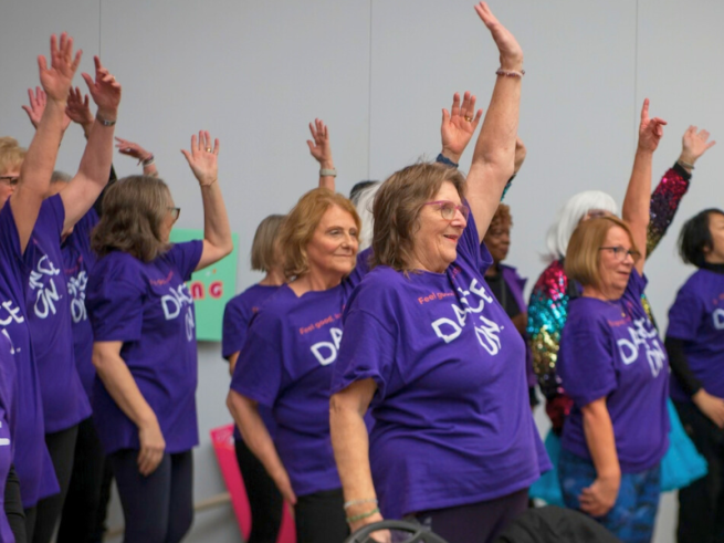A group of ladies in 'dance on' T-shirts are dancing with their arms in the air