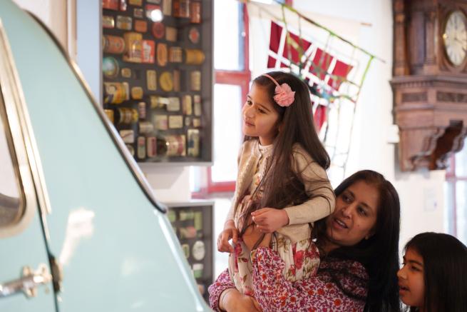 An adult lifting up a child to look at a car in the museum