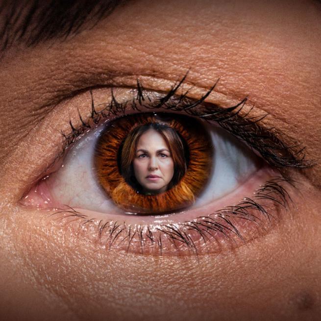 Close-up photo of someone's eye, with a woman's face reflecting in the pupil. 